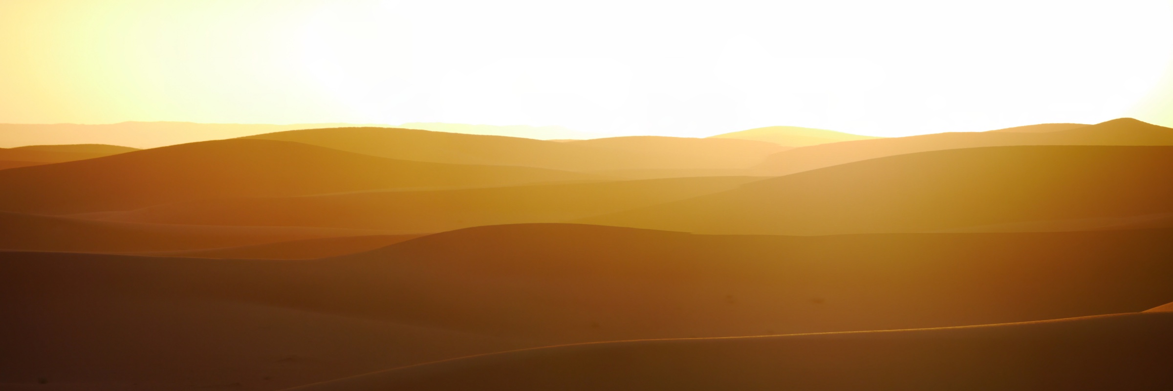Sand dunes receding into haze under a low sun.