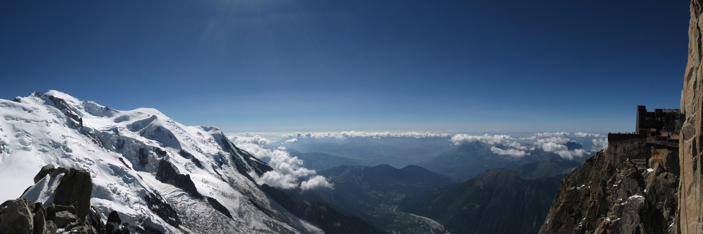 The Mont Blanc massif under snow, cloud filling the valley below, and the Aiguille du Midi terrace on the rock at right.